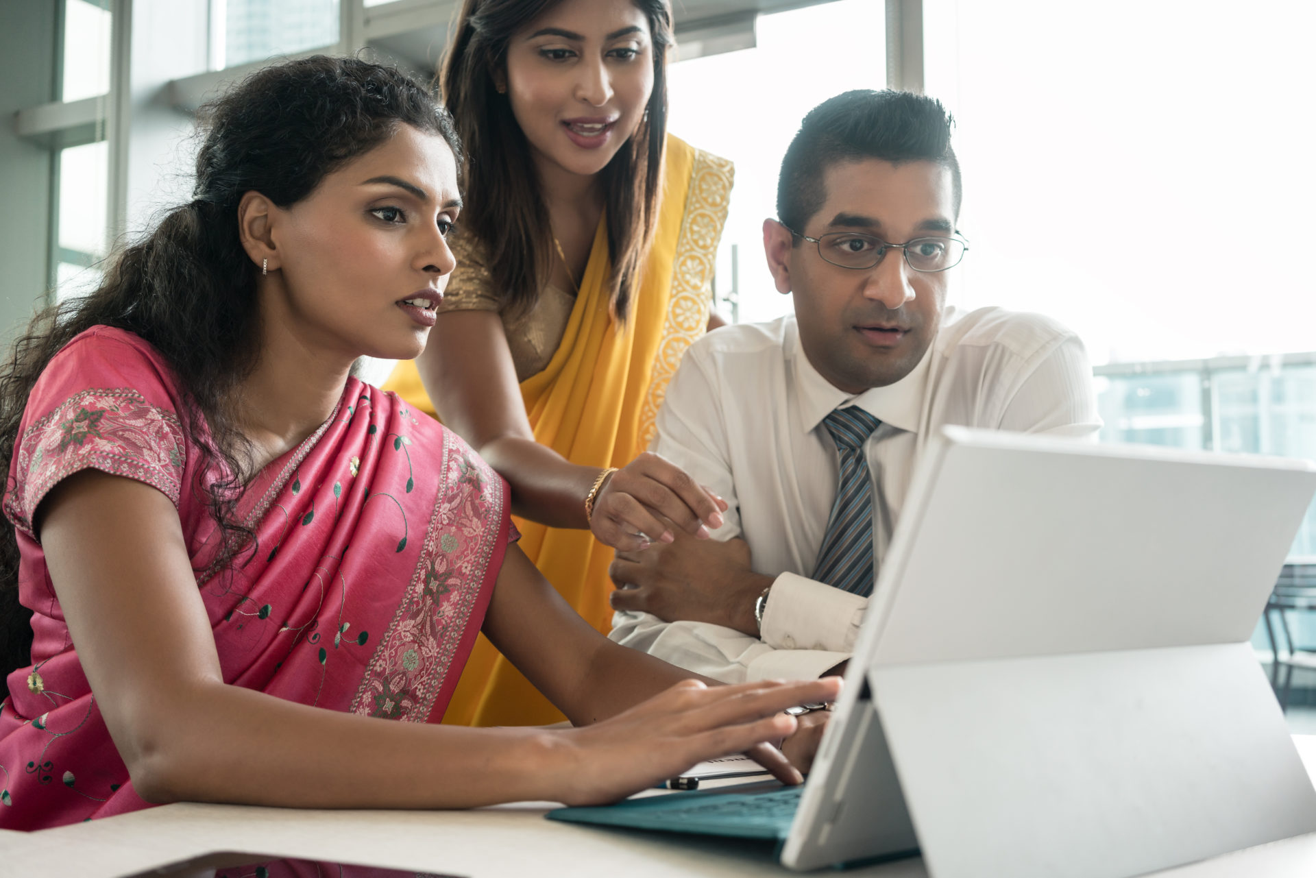 Three creative Indian employees working together around a laptop in a modern office