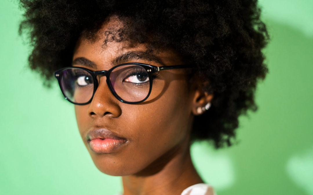 Close-up of woman wearing eyeglasses standing against green background
